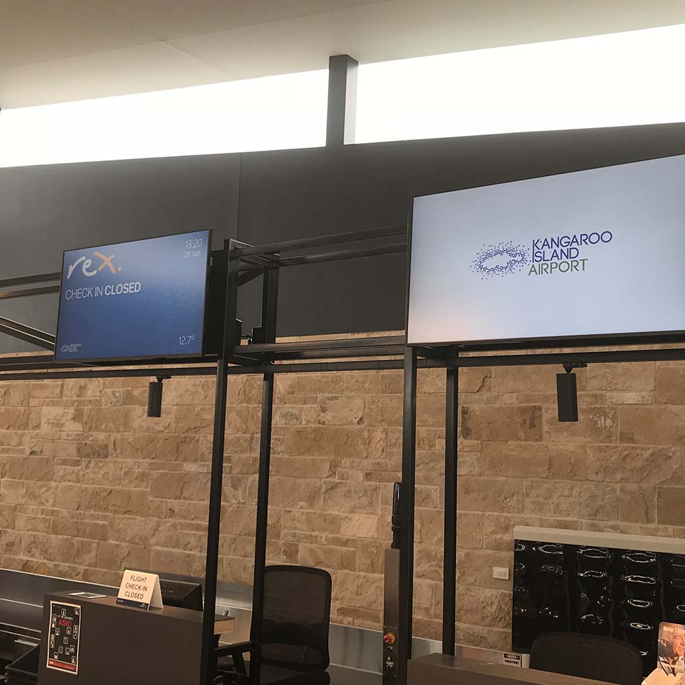 Check-in counter screens at Kangaroo Island Airport, one showing a Rex “Check in closed” message and the other the airport logo