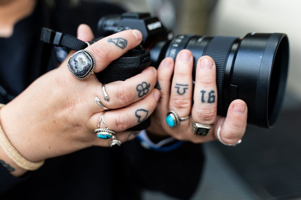 Tattooed hands with rings holding a camera