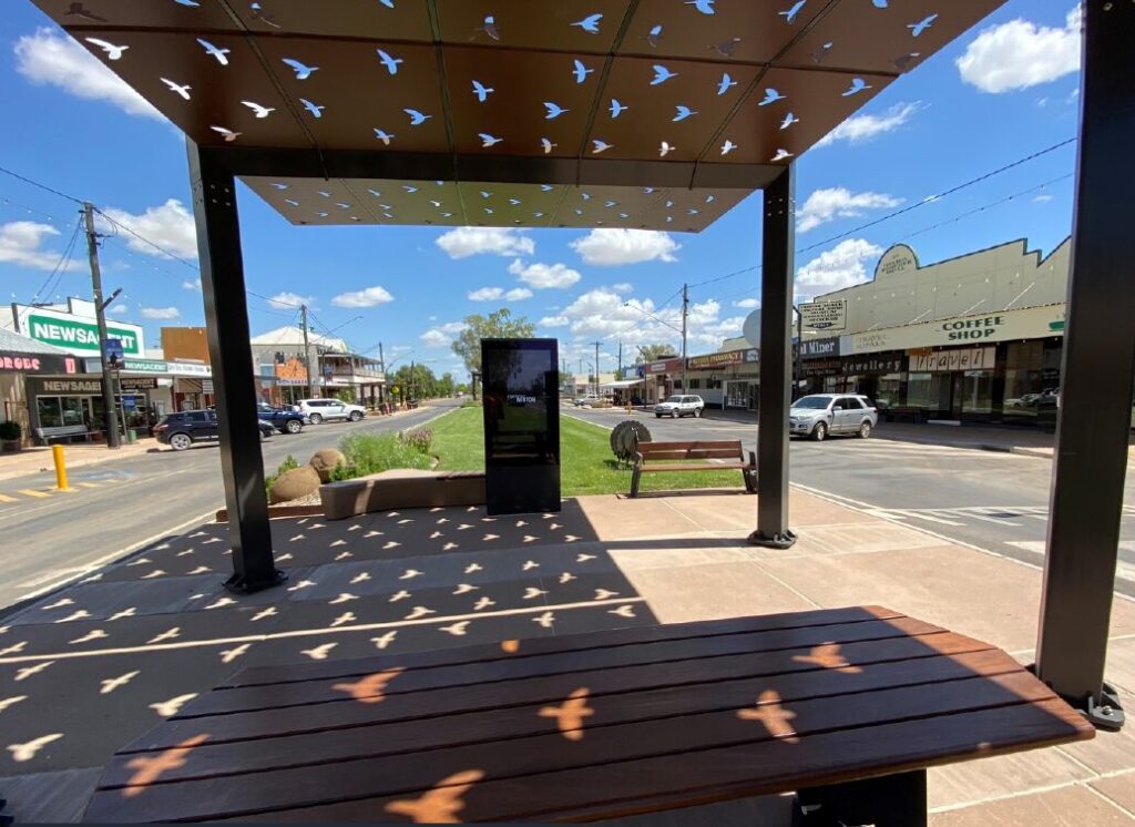 The outdoor touchscreen standing in the median of Elderslie Street, Winton, seen from a shade shelter with bird-shaped cut-outs
